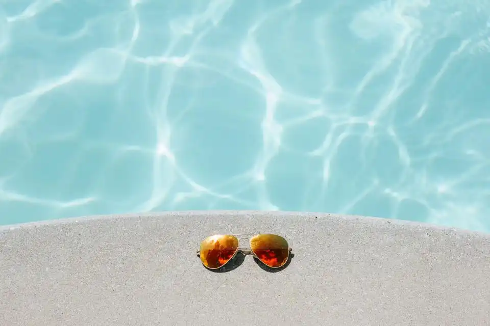 Água clara da piscina com óculos de sol na borda